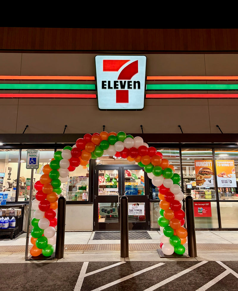 Red green and white balloon arch over a 7-Eleven storefront entrance, Spokane