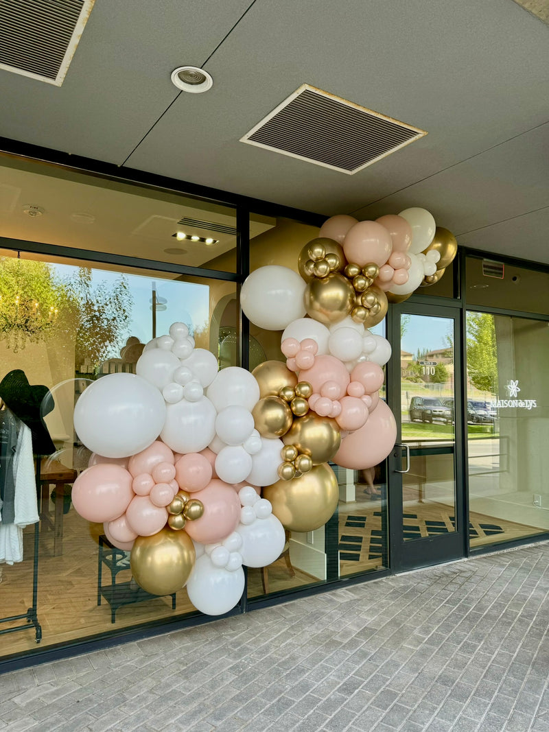 Blush pink and gold balloon garland on a wall behind a dessert table