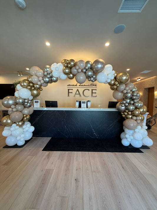 Organic gold and white balloon arch over a reception desk