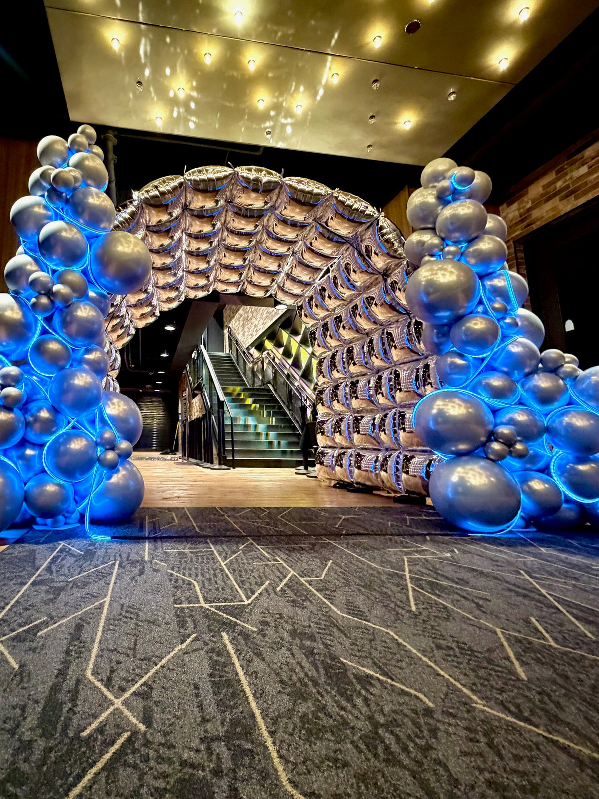 Large silver and blue balloon arch over an escalator entrance