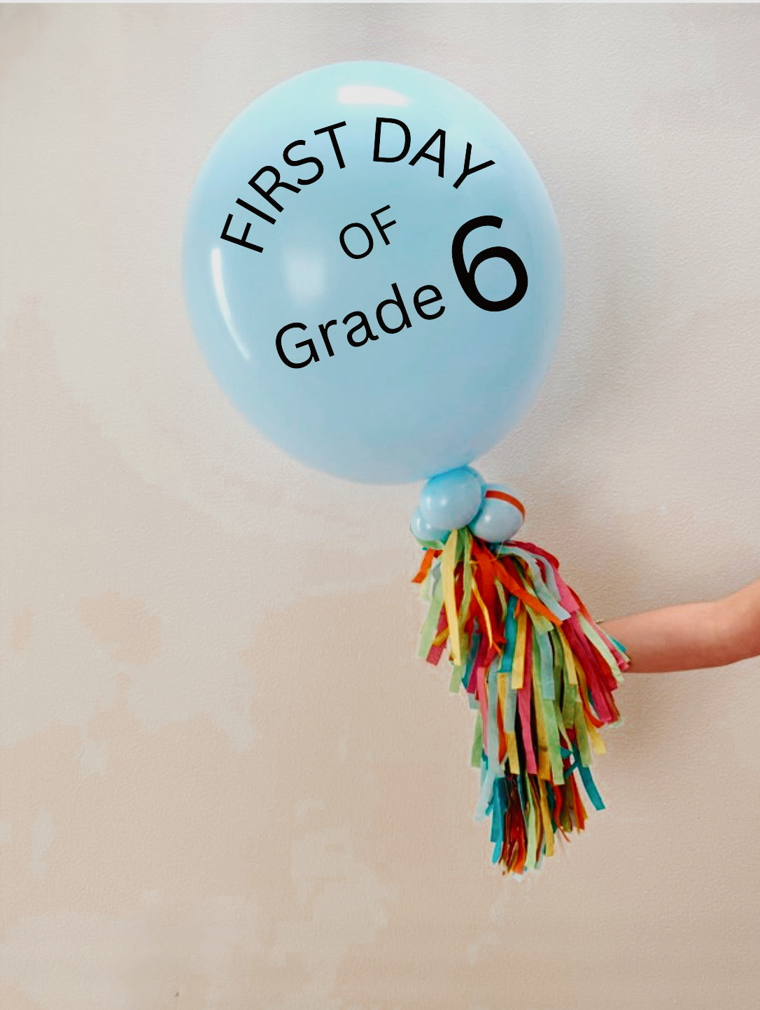Jumbo balloon with printed lettering and tassel tail, held for scale